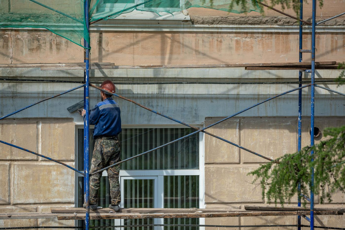 Contractor in hard hat repairing a building facade from scaffolding